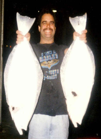 Stephen Speregen holding up 2 large Halibut fish, one in each hand